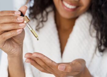 Smiling woman holding a dropper of facial serum above her open palm.