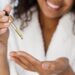 Smiling woman holding a dropper of facial serum above her open palm.